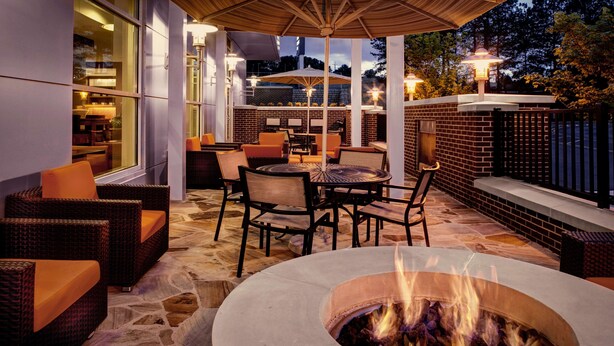 Une terrasse extérieure avec un foyer, des meubles en osier et des murs en briques.