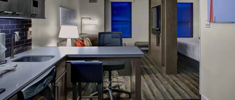 A compact hotel room with a kitchenette, a dining area, a bed, and a TV.