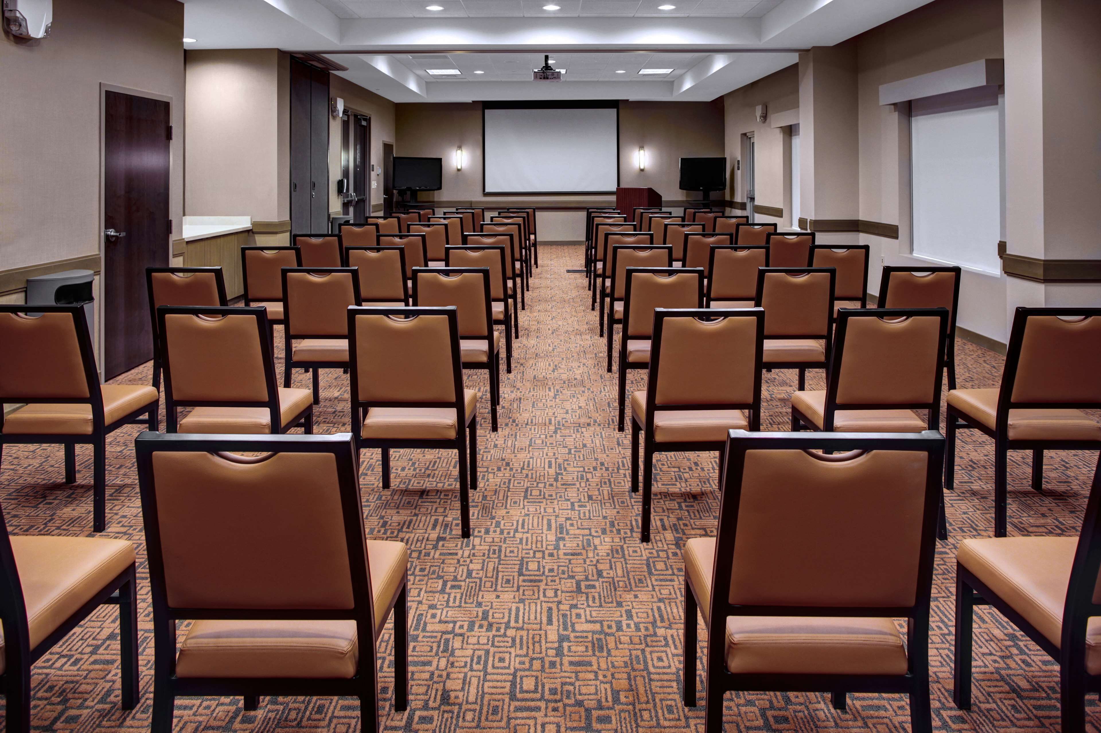 A conference room with rows of chairs, a projector screen, and two televisions.