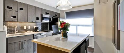 A modern kitchen with grey cabinets, a central island, and a hanging light fixture.
