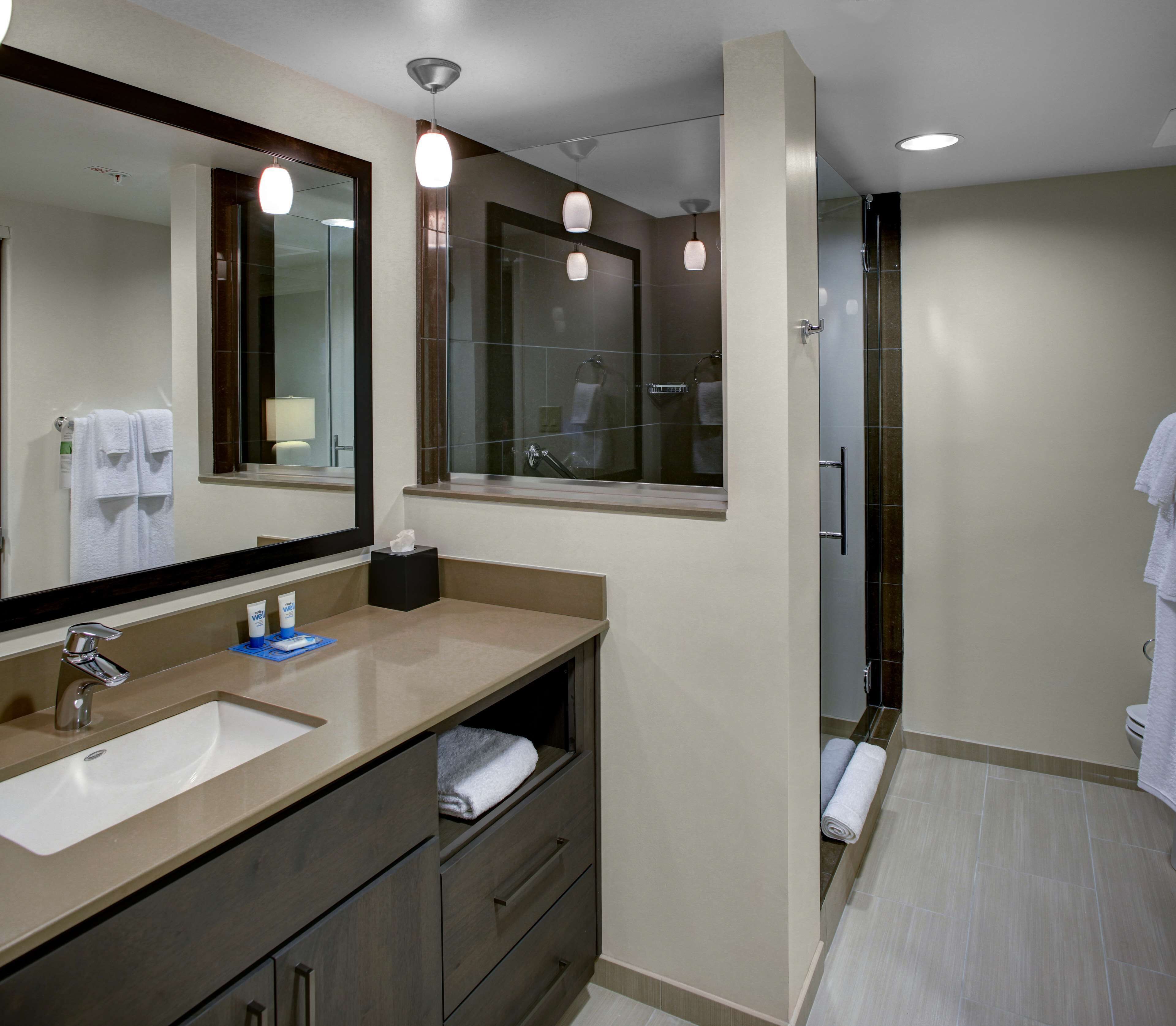 Un baño moderno con un espejo grande, un lavabo y una zona de ducha.