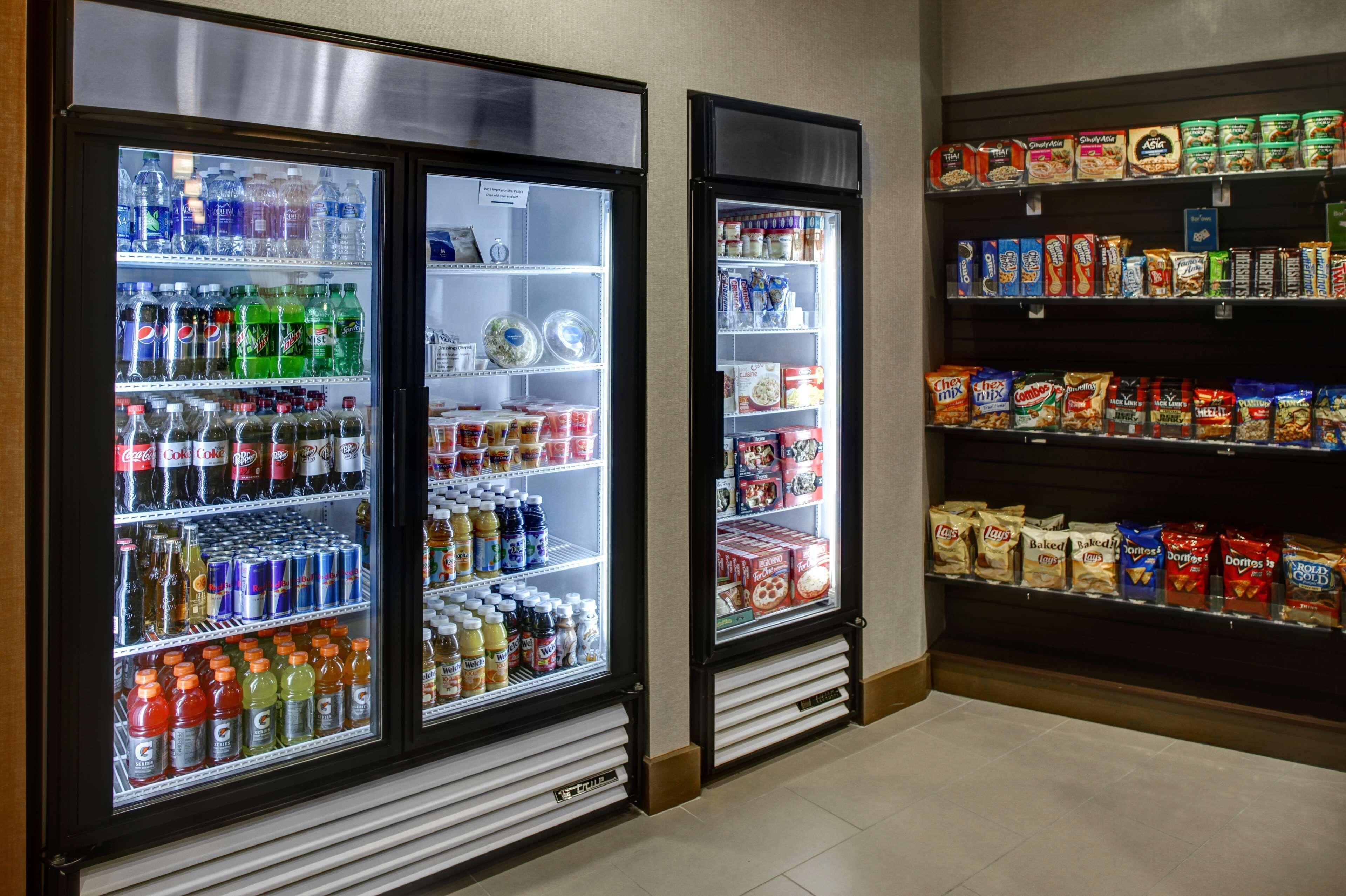 Un área de venta con dispensadores de bebidas refrigeradas y estantes llenos de aperitivos y alimentos.