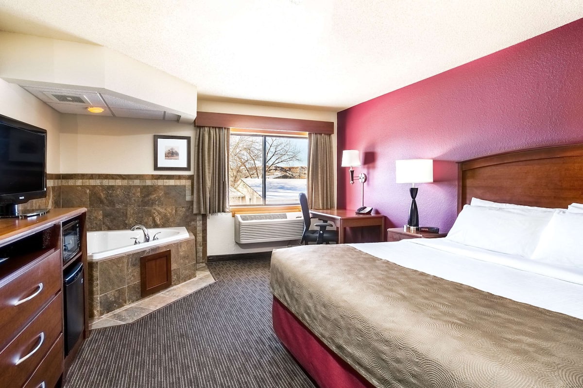 Habitación de hotel con cama, escritorio, silla, televisor, baño con lavamanos y bañera, y ventana con vista al exterior.