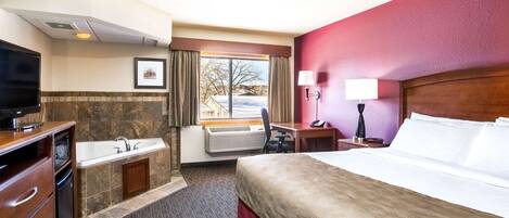 Habitación de hotel con cama, escritorio, silla, televisor, baño con lavamanos y bañera, y ventana con vista al exterior.