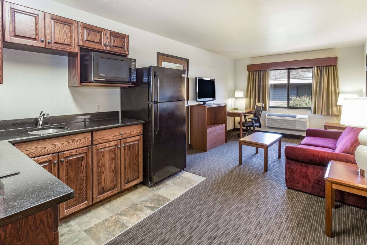 Una habitación de hotel compacta con kitchenette, televisión de pantalla plana, sofá y una pequeña mesa.