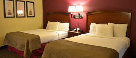 A hotel room with two beds, a nightstand with a lamp, and three framed pictures on the wall.