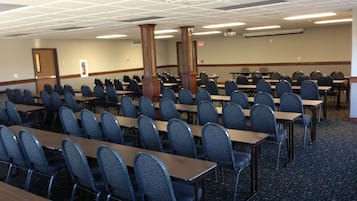 A conference room with rows of tables and chairs, a large pillar, and a carpeted floor.
