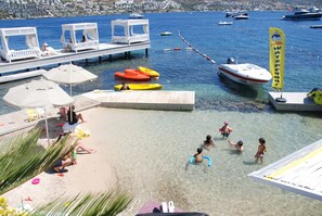 Una playa con agua cristalina, un muelle con sillas de descanso y barcos.