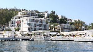 Hotel aan het water met meerdere balkons, zitplaatsen buiten en een steiger met ligstoelen.
