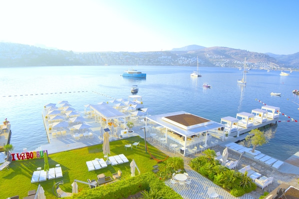 Un hotel frente al mar con terraza, piscina y barcos al fondo.