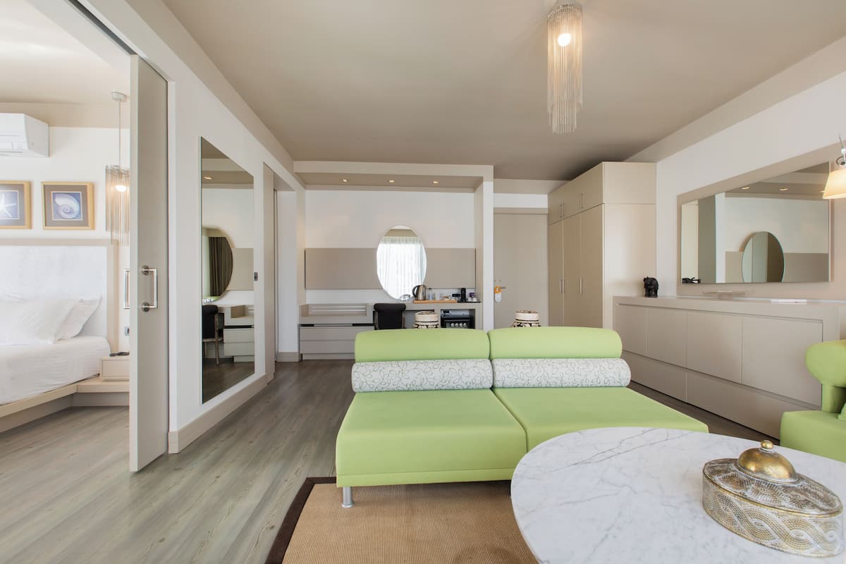 Ein modernes Hotelzimmer mit einem grünen Sofa, einem weißen Bett, einem Marmorkaffeetisch und einer Küchenzeile mit einem großen Spiegel.