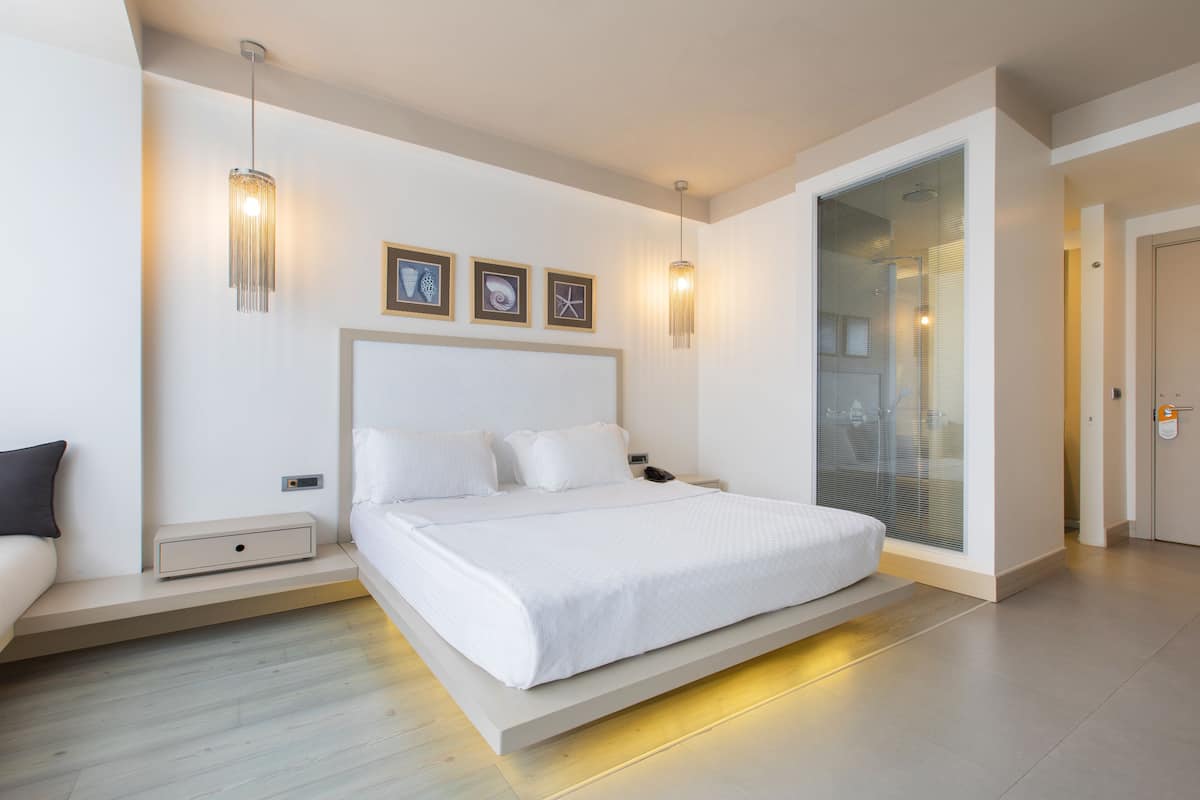 Ein modernes Schlafzimmer mit einem großen Bett, Nachttischen, einer Nachttischlampe und einer Glastür zum Badezimmer.