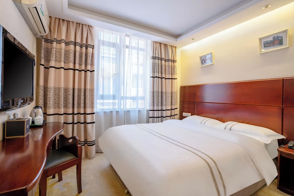 A hotel room with a large bed, a desk with a chair, a flat-screen TV, and curtains.
