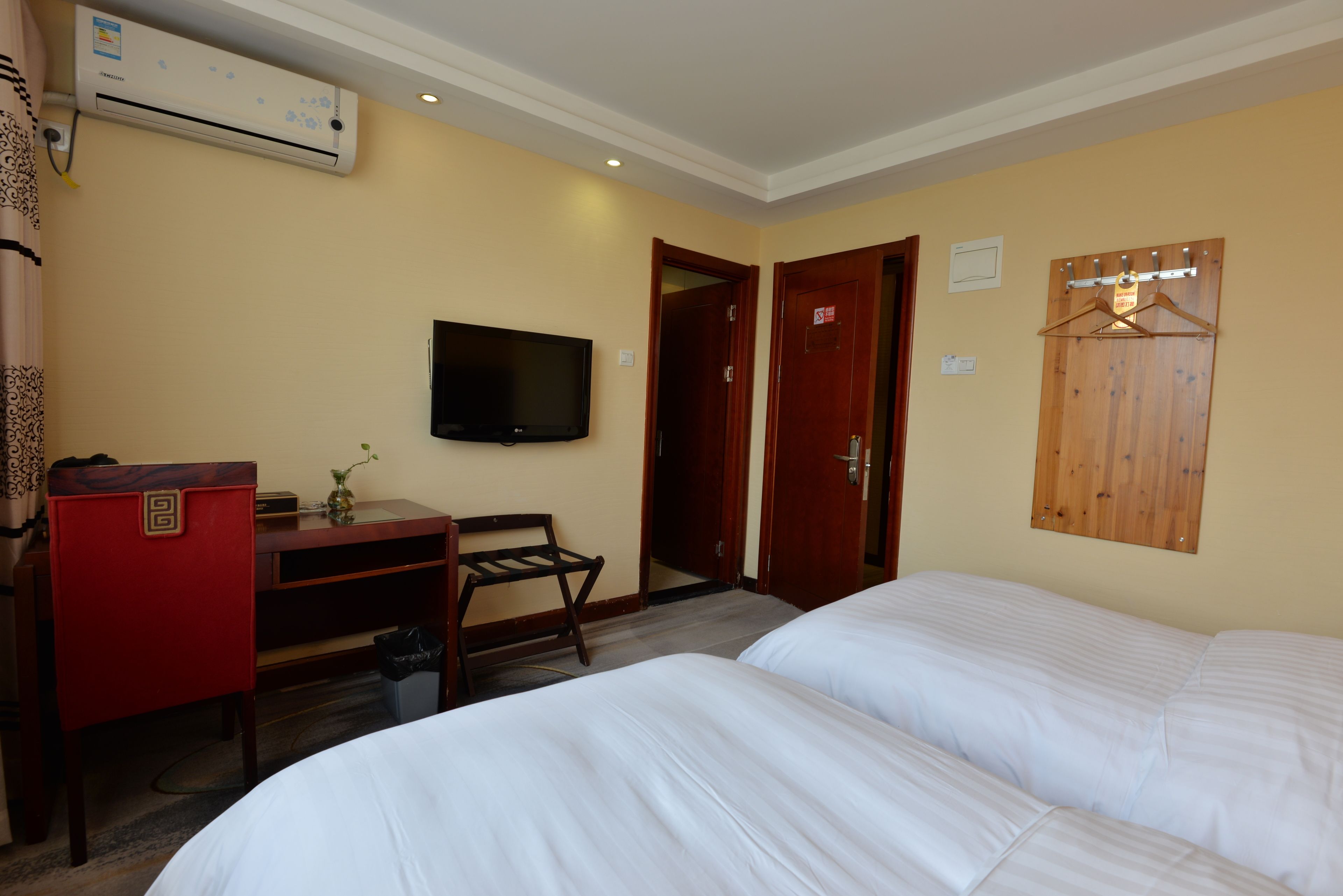 A hotel room with two beds, a desk, a television, and a wooden coat rack.