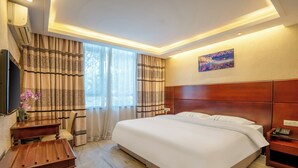 Une chambre d’hôtel avec un grand lit, un bureau, une chaise, une télévision et un tableau au mur.