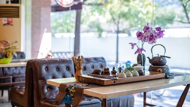 L’intérieur chaleureux d’un restaurant, avec une table en bois, une théière ancienne et un vase rempli d’orchidées violettes.