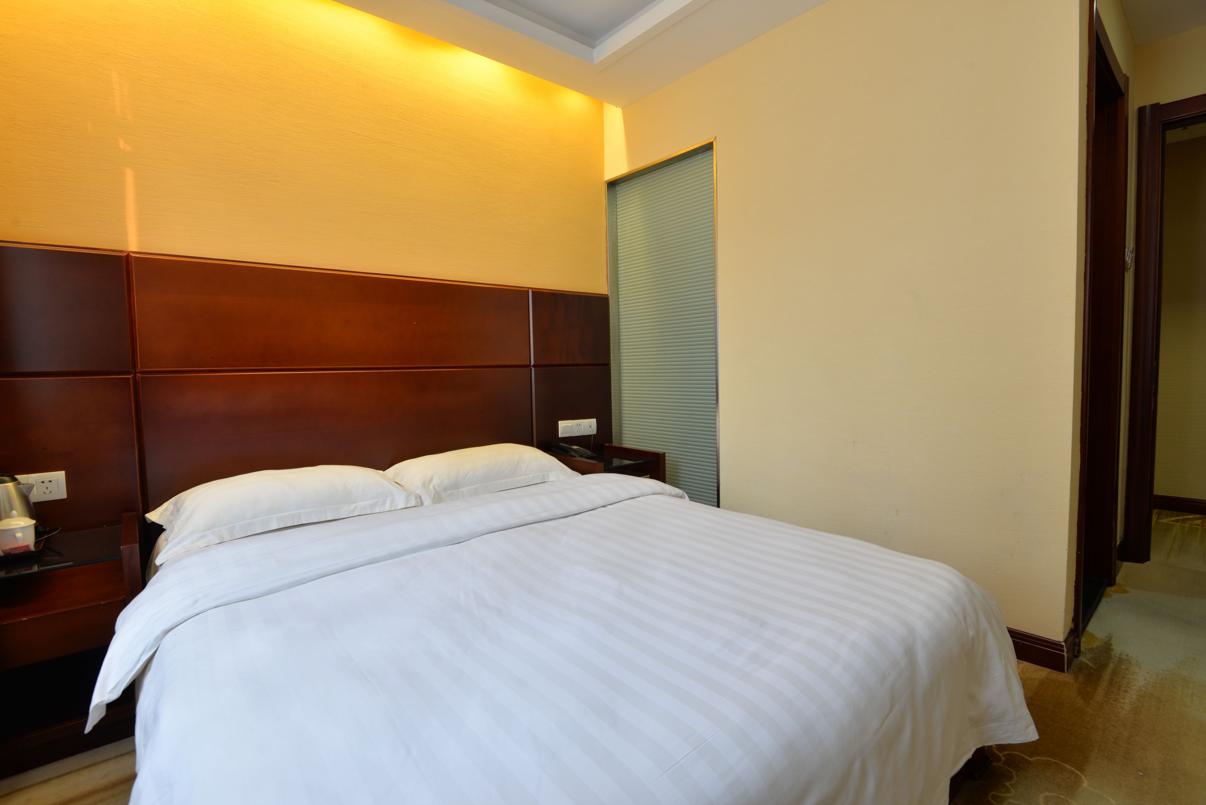 A hotel room with a large bed, wooden headboard, bedside table, and a nightstand.