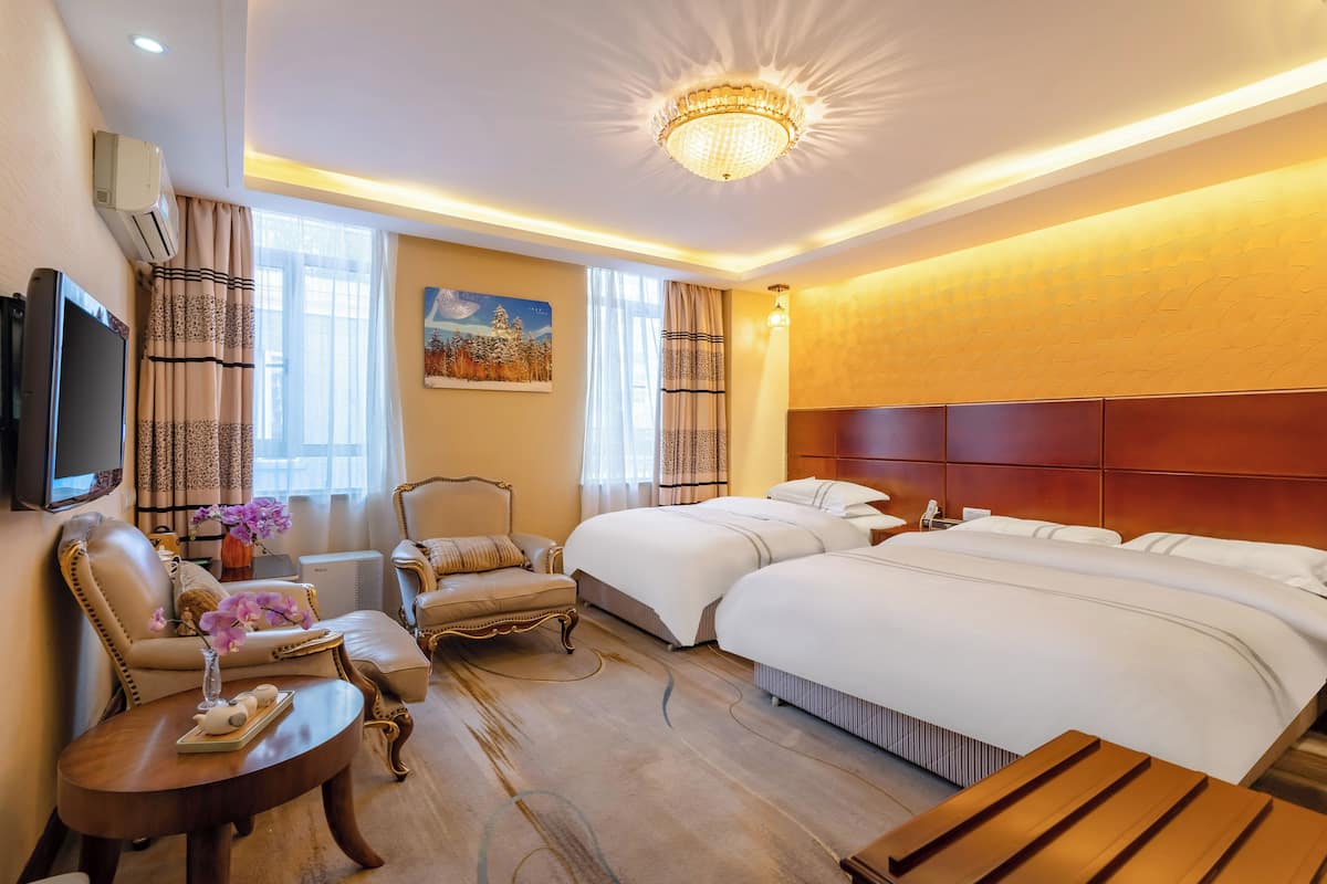 A hotel room with a large bed, a sofa, a chair, a TV, and a chandelier.