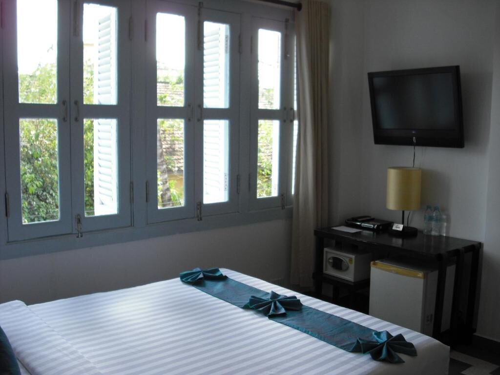 Una camera d'albergo con un letto, una scrivania con lampada, una televisione e una finestra con persiane.