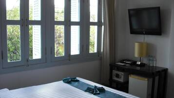 Una camera d'albergo con un letto, una scrivania con lampada, una televisione e una finestra con persiane.