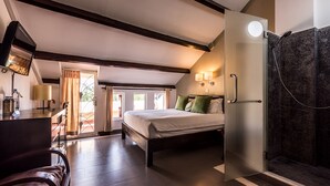 A bedroom with a bed, a desk, a chair, a shower, and a view of the outdoors. - The Columns (Kampot)