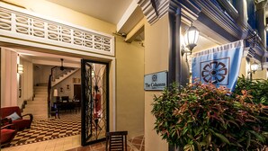 A hotel lobby with a checkered floor, a staircase, a red armchair, and a sign reading "The Columns". - The Columns (Kampot)