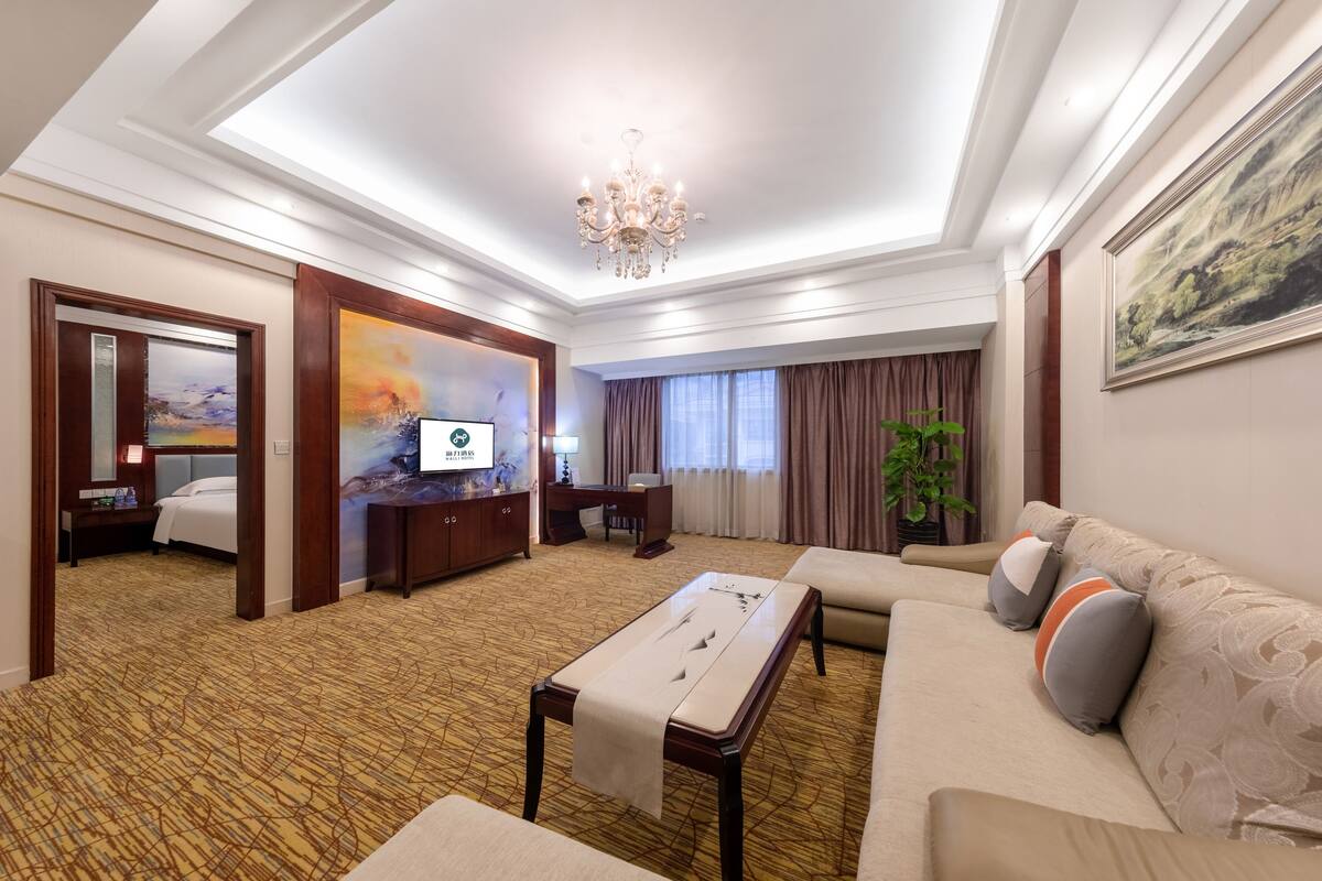 A hotel room with a large bed, a sofa, a desk, a TV, and a chandelier.