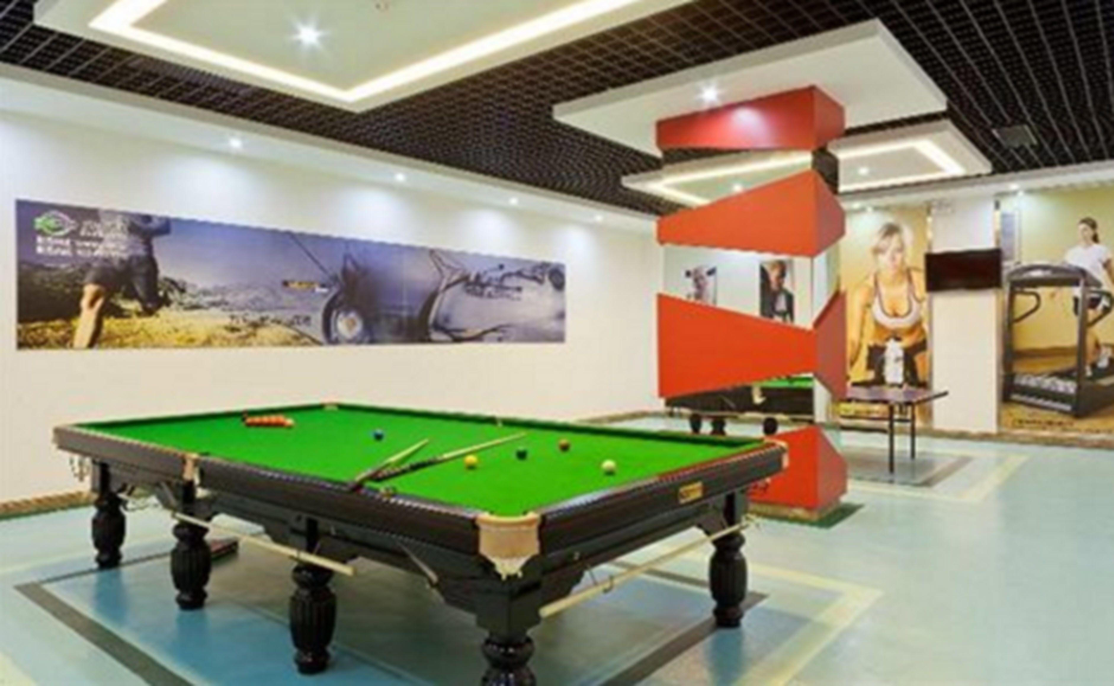 A pool table in a well-lit indoor area with a modern ceiling design and a large poster on the wall.