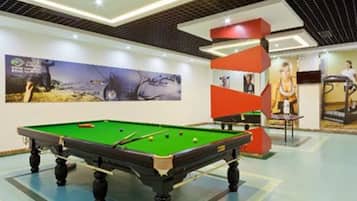 A pool table in a well-lit indoor area with a modern ceiling design and a large poster on the wall.