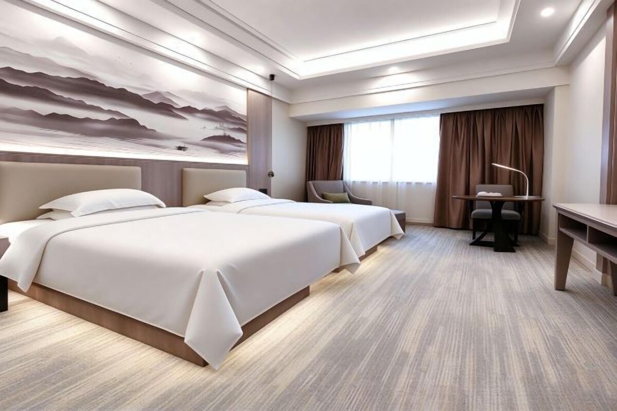 A hotel room with two beds, a desk, and a large window with curtains.