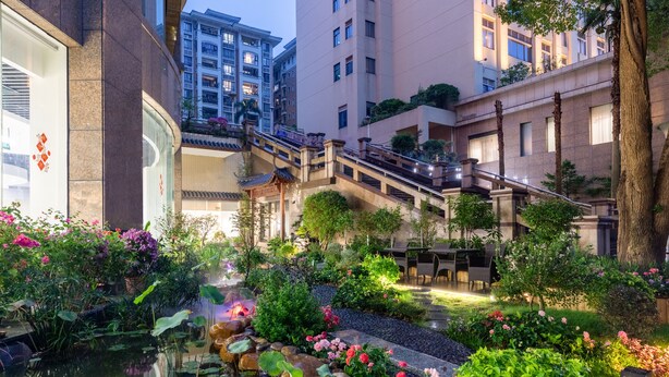 Un patio con estanque de carpas, abundante vegetación y un puente tradicional.
