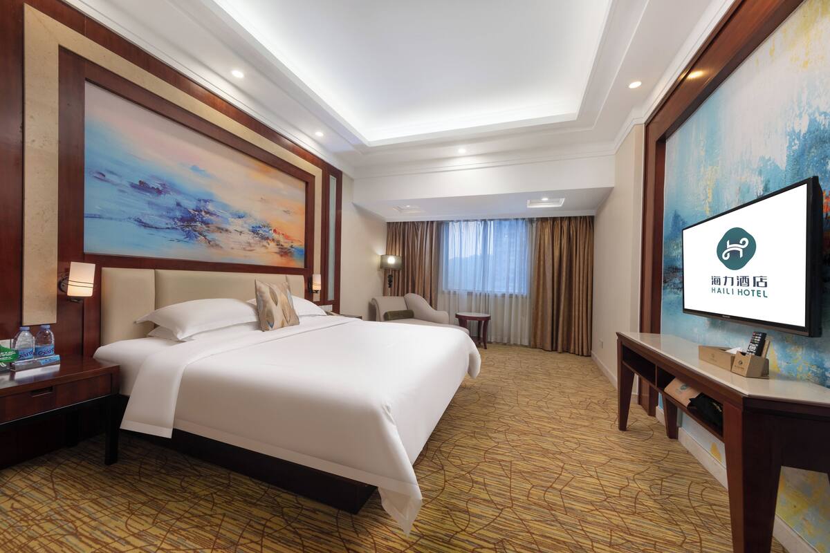 A hotel room with a large bed, a desk, a TV, and a painting on the wall.