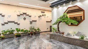 Un interior moderno con piso de concreto pulido, decoración mural tradicional y un espejo grande que refleja un bonsái.