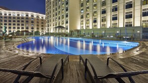 Una amplia piscina cubierta con sillones de descanso y una zona de estar techada, rodeada por un edificio de hotel de varios pisos.