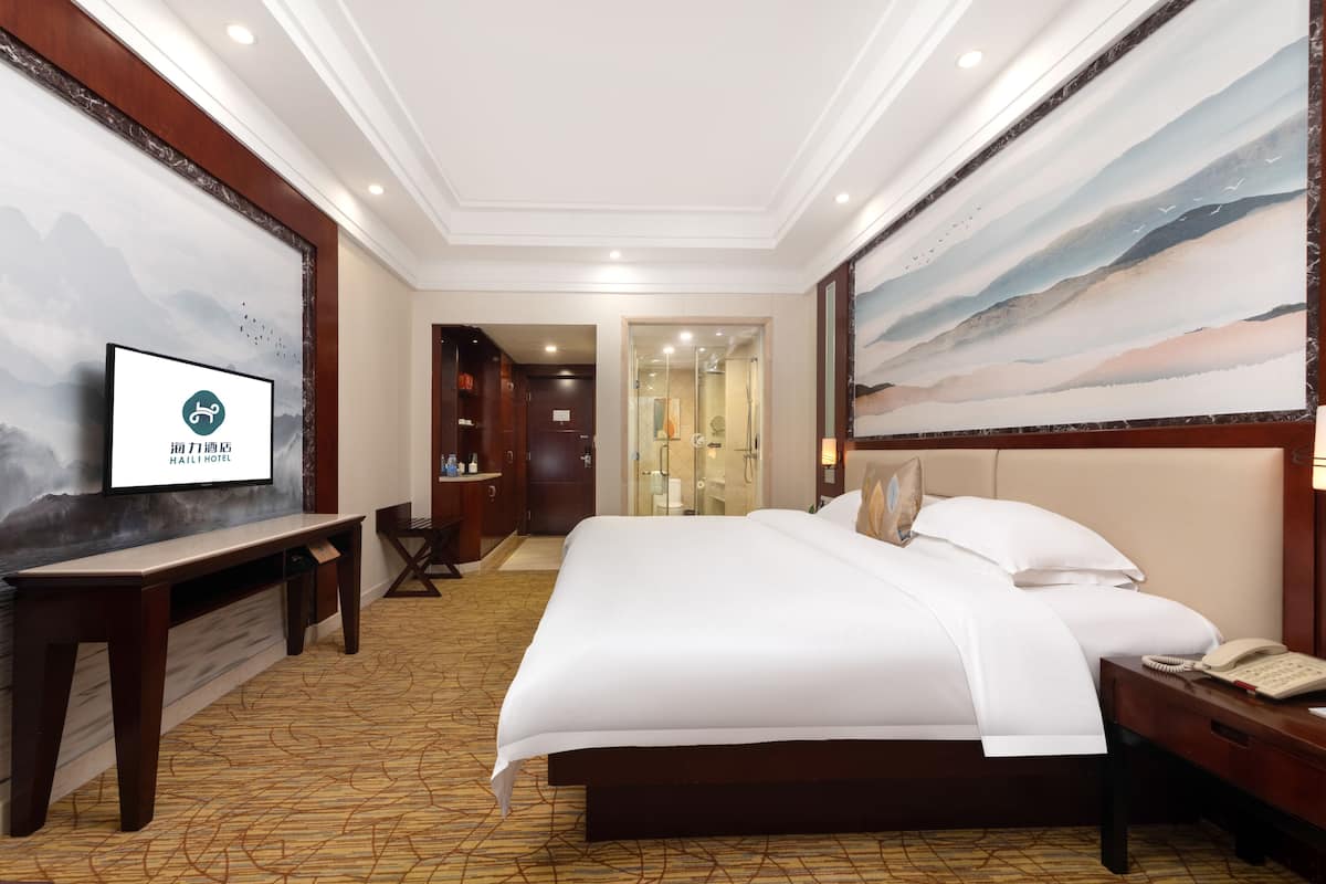 A hotel room with a large bed, a desk, a TV, and a painting on the wall.