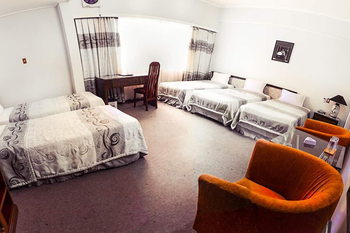 A hotel room with two beds, a desk, a chair, a TV, and a small table with a lamp.
