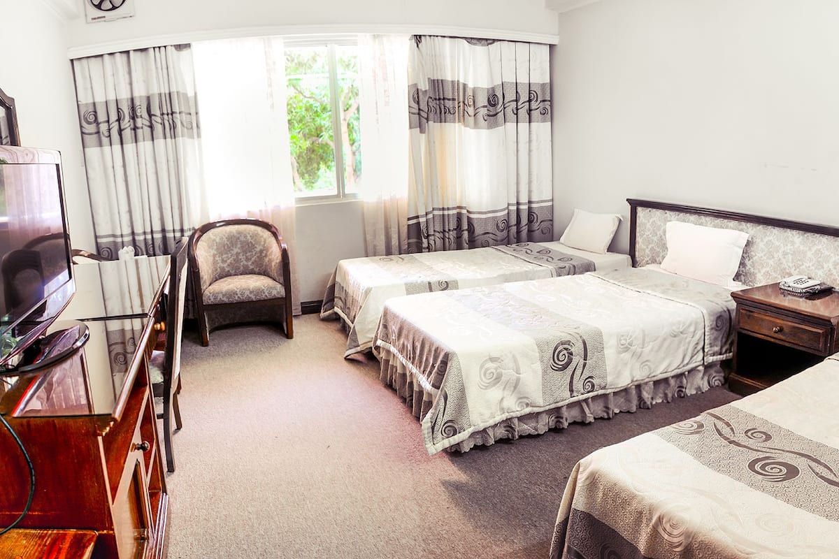 A hotel room with two single beds, a chair, a TV, and a bedside table with a phone.