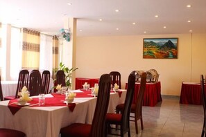 A dining area with tables set for a meal, chairs, and a painting on the wall. - Ban Mê Dakruco Hotel (Nha Trang)