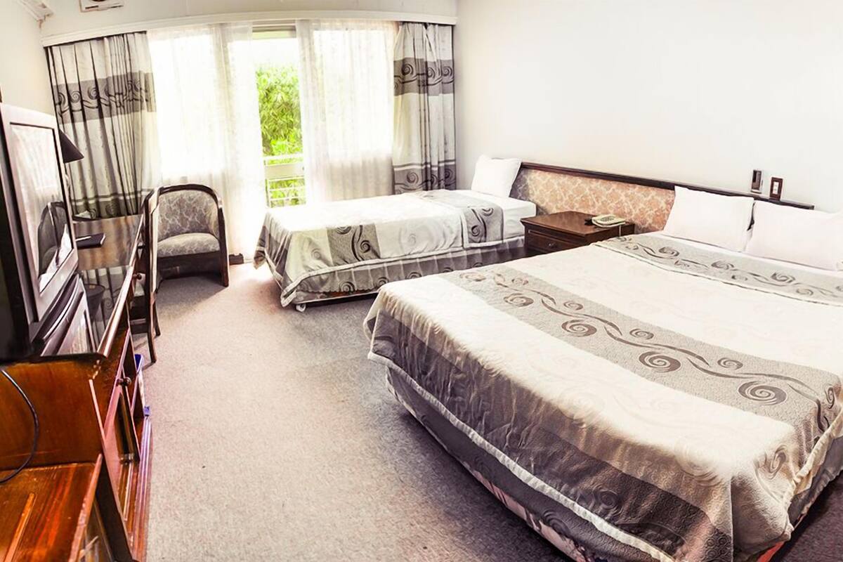 A hotel room with two beds, a desk, a chair, and a window with curtains.