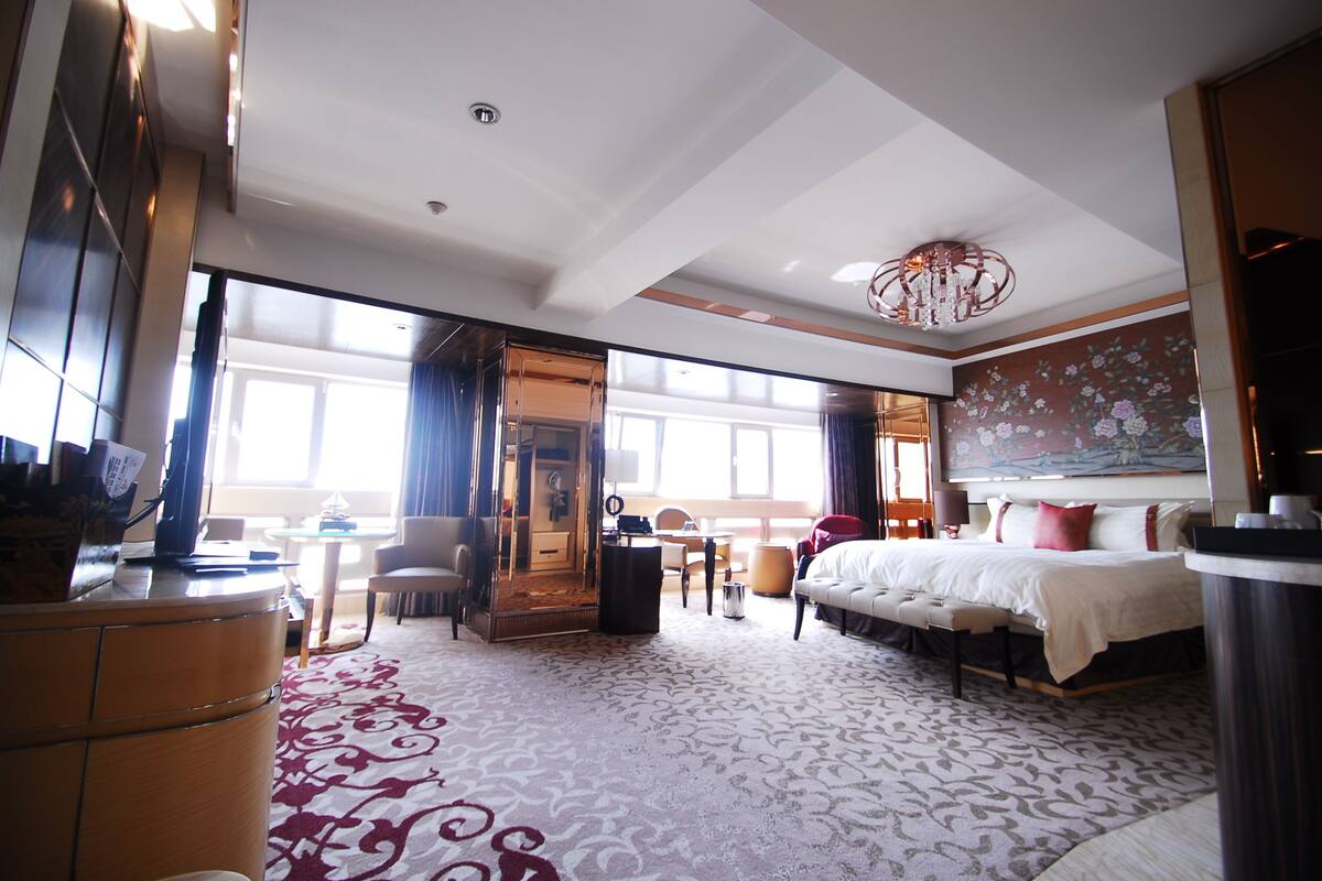 Ein Hotelzimmer mit einem großen Bett, einem Schreibtisch, einem Sessel, einem Spiegel und einem Teppichboden.