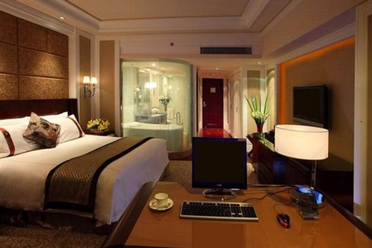 Ein Hotelzimmer mit Bett, Schreibtisch mit Computer, Fernseher und einem durch eine Glastür sichtbaren Badezimmer.