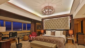 A spacious hotel room with a large bed, a desk, a television, and a view of the city at night. - Shandong Hotel (Jinan)