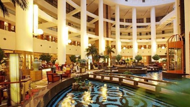 A multi-level hotel lobby with a central water feature, multiple floors, and a variety of seating areas. - Shandong Hotel (Jinan)