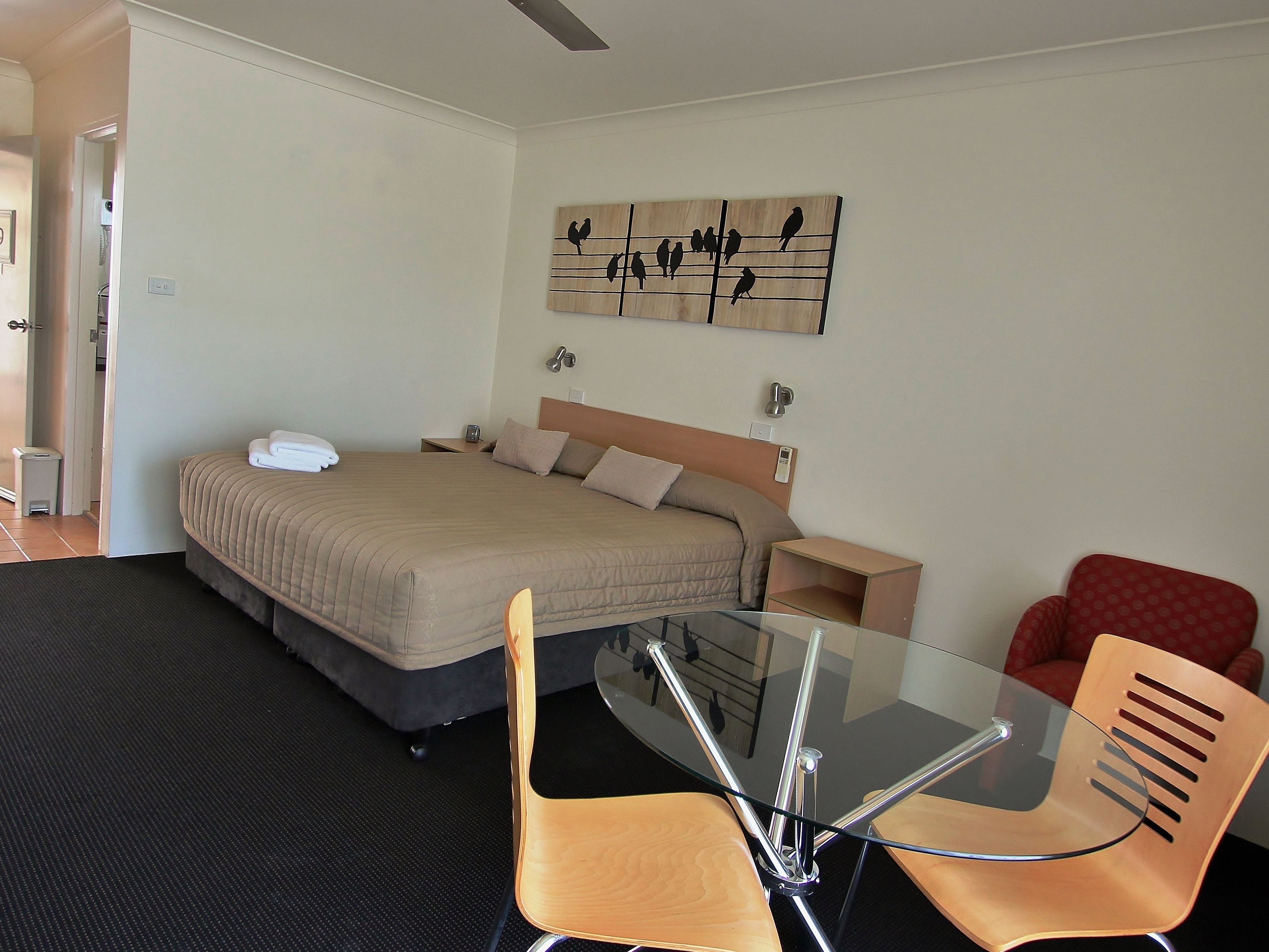 Ein Hotelzimmer mit Bett, Nachttischen, einem Glastisch mit Stühlen, einem roten Sessel und einem Wandbild.
