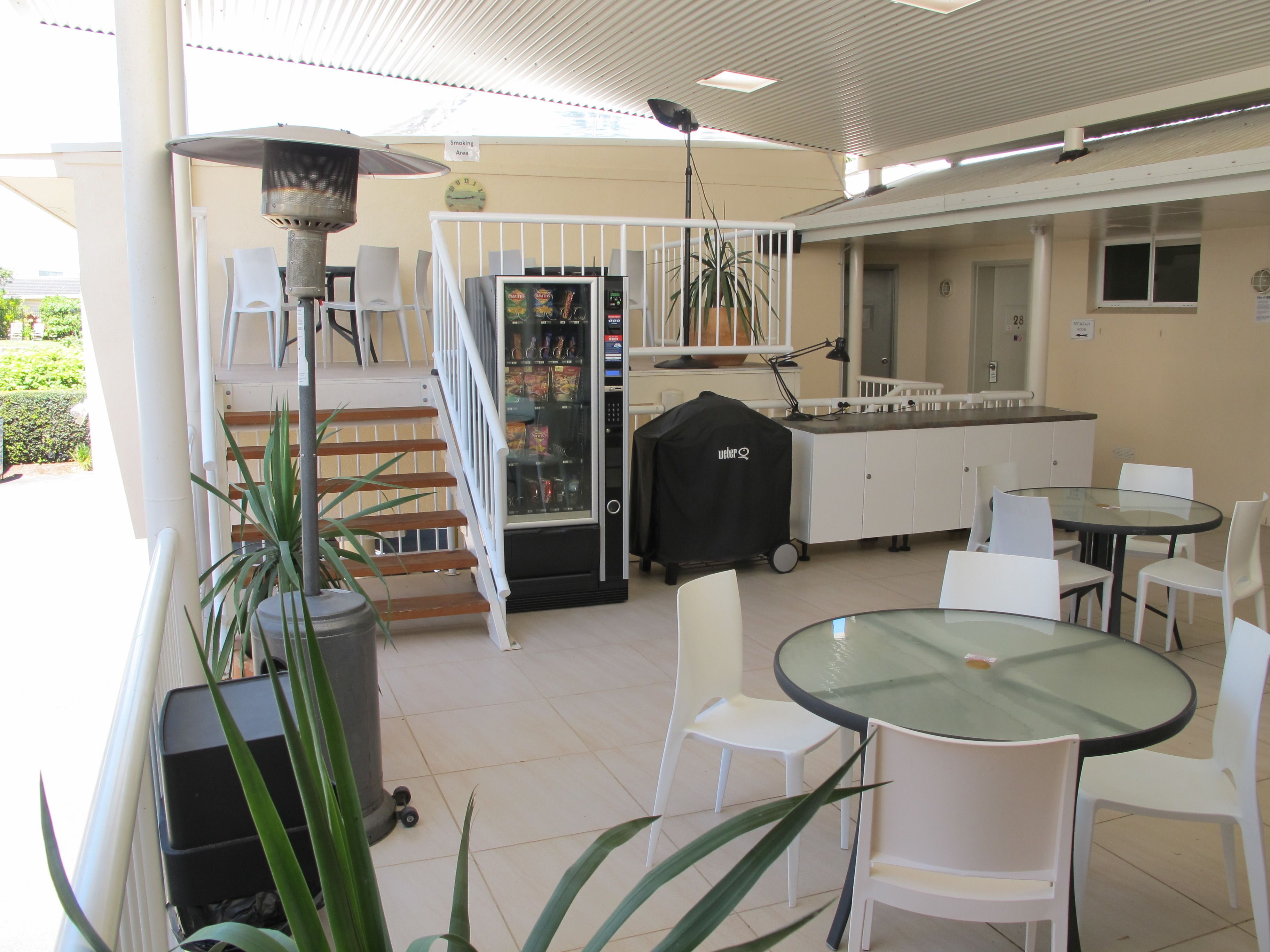 A covered outdoor area with a vending machine, a grill, and seating arrangements.