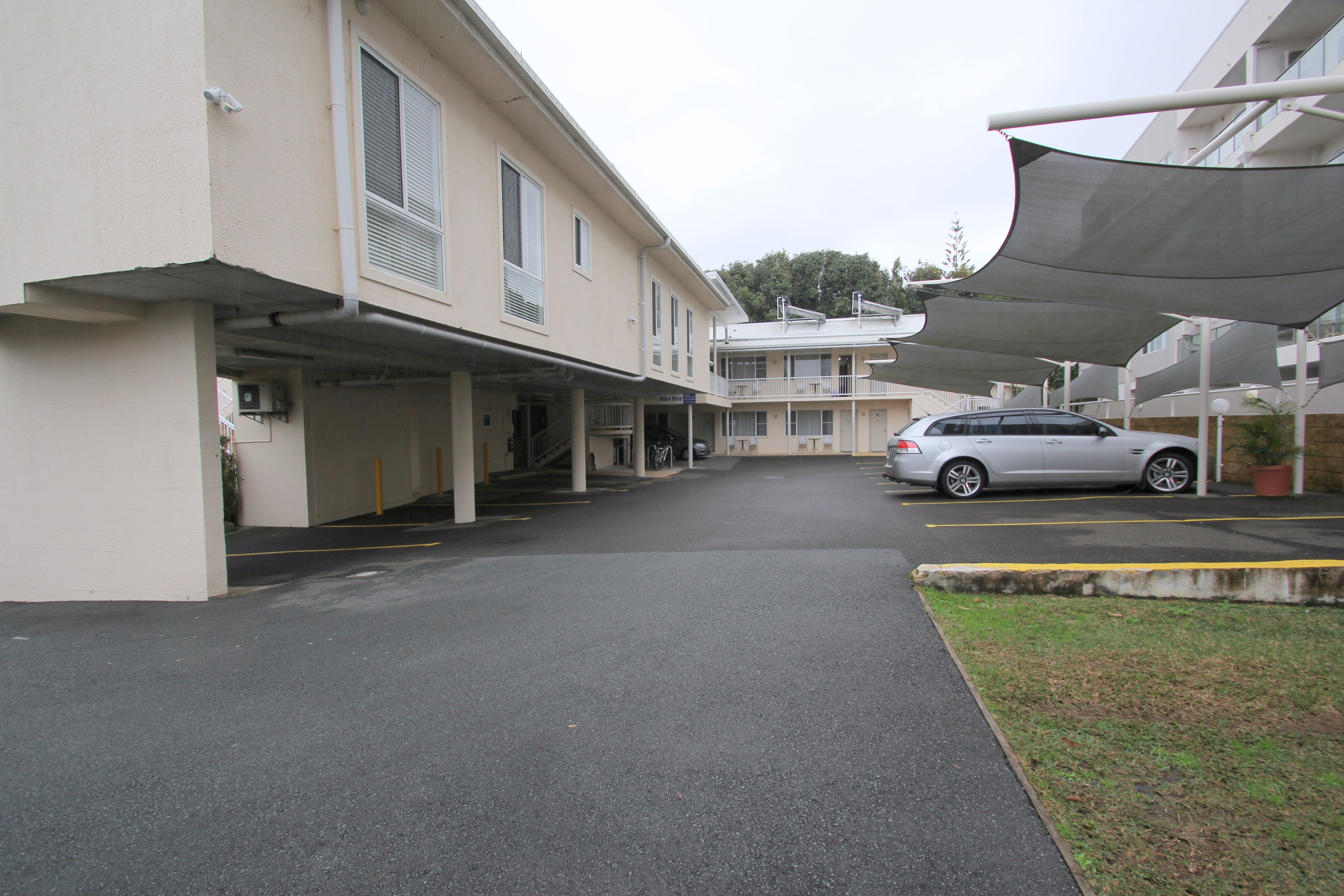 A parking area with a covered walkway leading to a building with multiple floors and balconies.