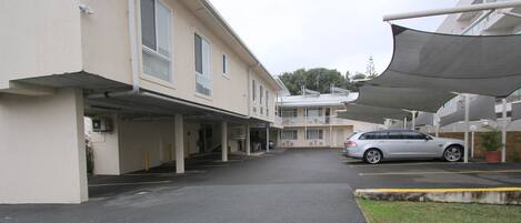 A parking area with a covered walkway leading to a building with multiple floors and balconies.