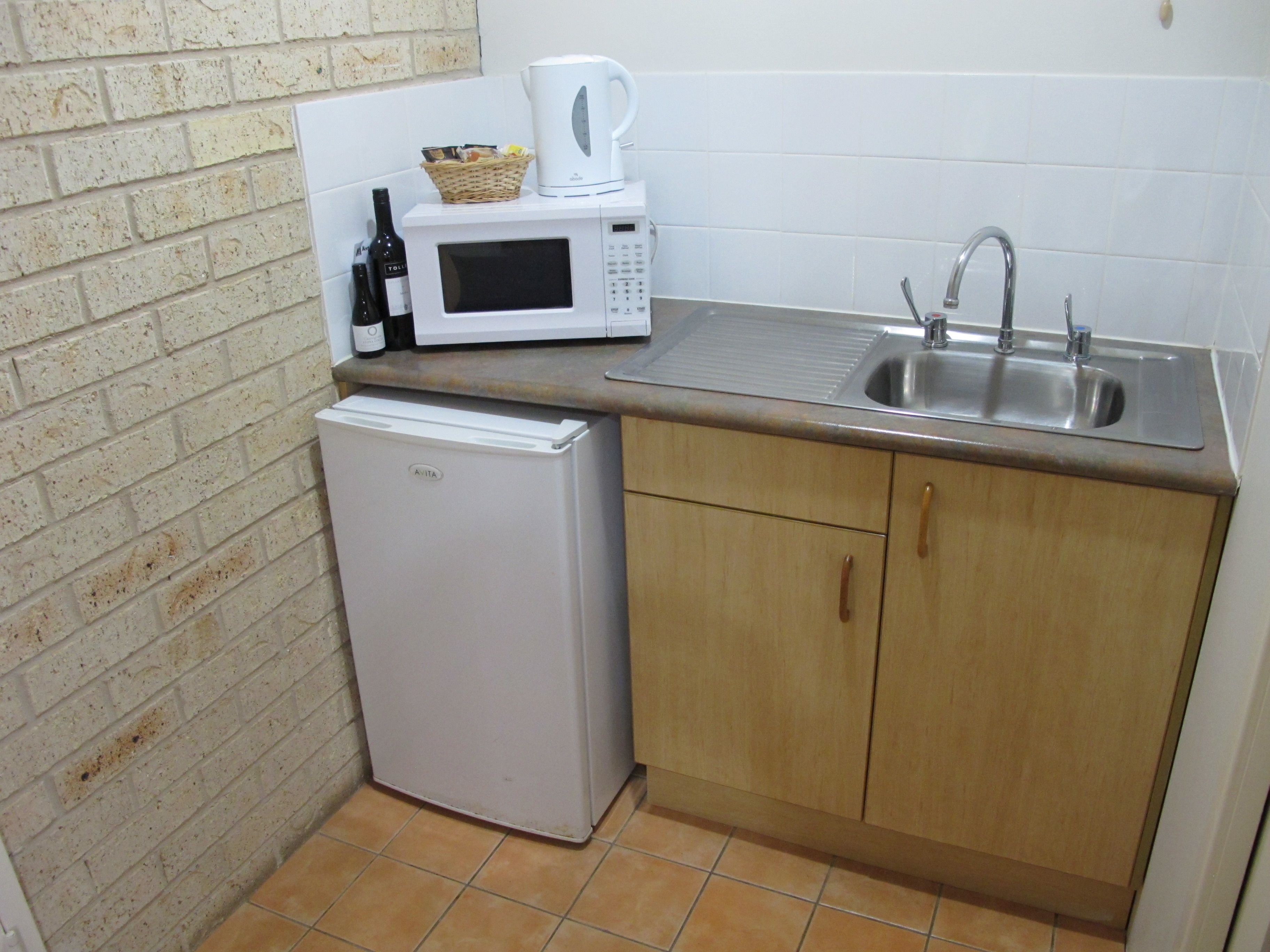 A compact kitchen with a white refrigerator, a microwave, a sink, and a small cabinet.