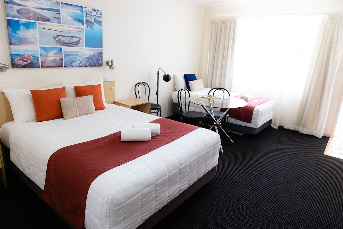A hotel room with a large bed, a desk, a chair, and a small table.