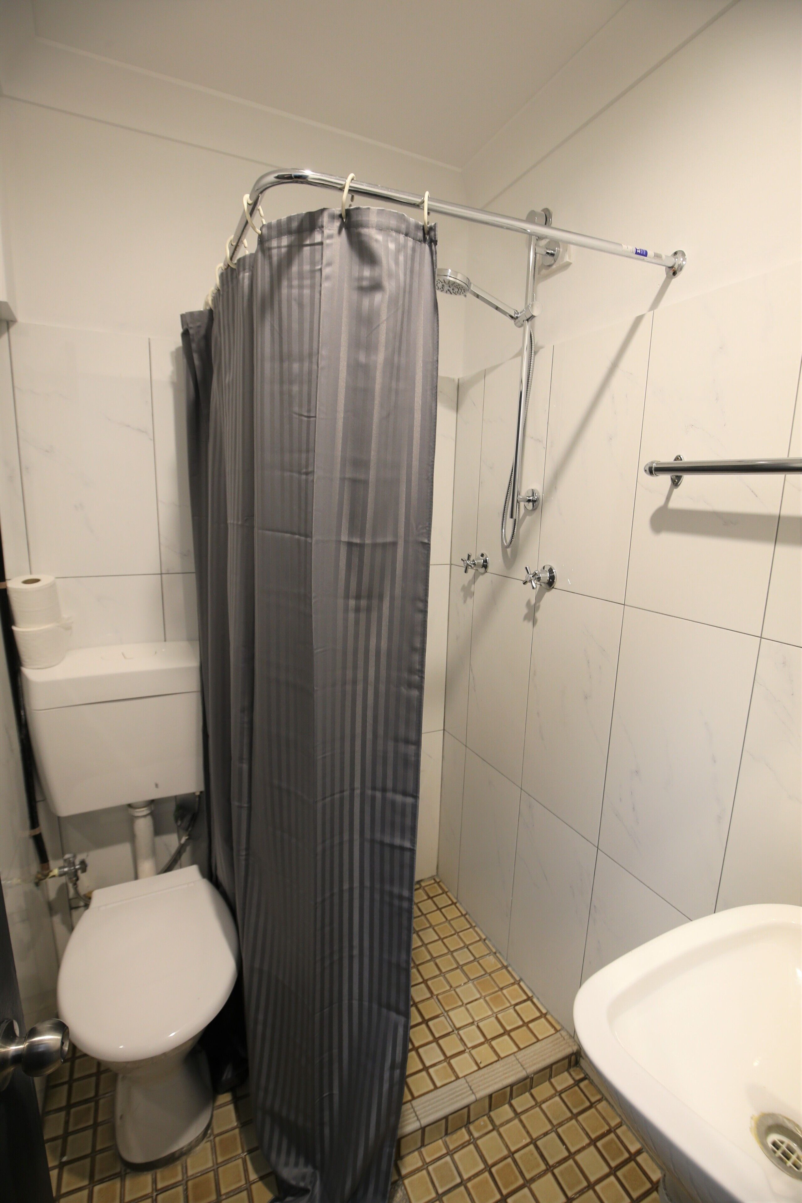 Pieni kylpyhuone, jossa on wc, suihku, jossa on suihkuverho, ja pesuallas.